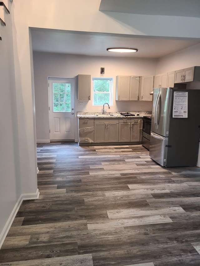 kitchen featuring appliances with stainless steel finishes, light stone counters, sink, gray cabinets, and dark wood-type flooring