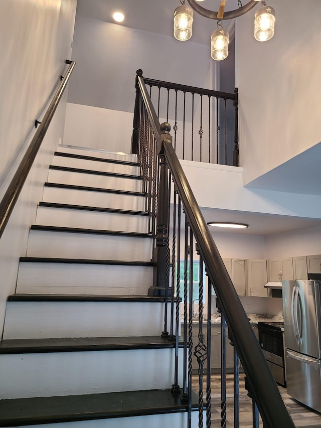 staircase with a high ceiling, wood-type flooring, and a chandelier