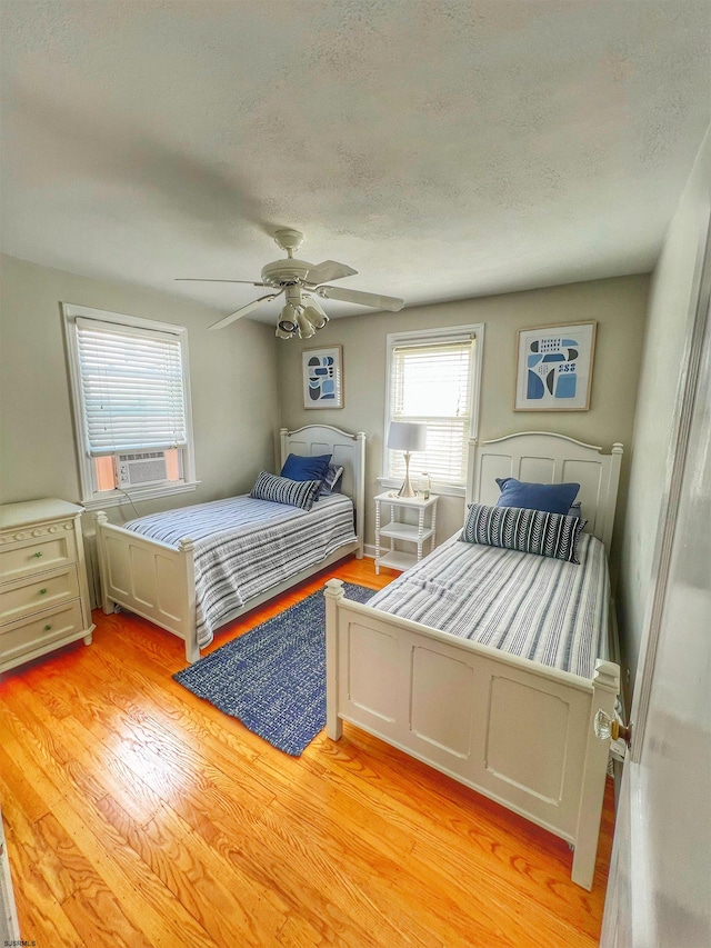 bedroom with light wood-type flooring, ceiling fan, cooling unit, and a textured ceiling