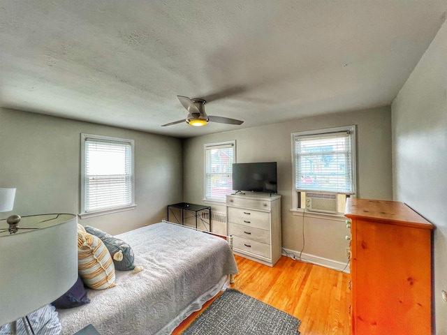 bedroom featuring ceiling fan, radiator heating unit, multiple windows, and light hardwood / wood-style floors