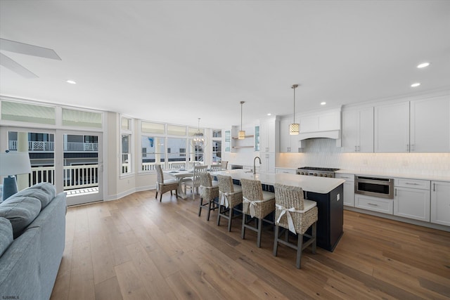 kitchen with a center island with sink, a breakfast bar area, hardwood / wood-style floors, and white cabinets