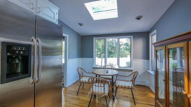 dining room with baseboard heating, vaulted ceiling with skylight, and light hardwood / wood-style floors