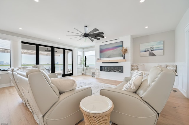 living room featuring french doors, light hardwood / wood-style flooring, ceiling fan, and a large fireplace