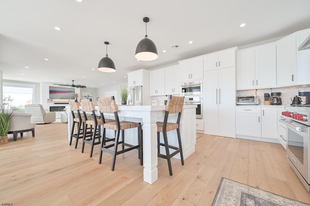 kitchen with a kitchen island, appliances with stainless steel finishes, hanging light fixtures, white cabinetry, and light wood-type flooring