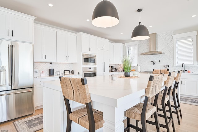 kitchen featuring light hardwood / wood-style flooring, appliances with stainless steel finishes, a kitchen bar, wall chimney range hood, and white cabinets