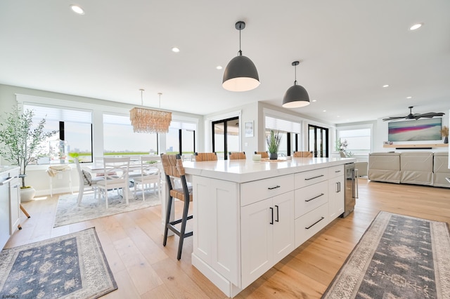 kitchen featuring light hardwood / wood-style floors, a center island, hanging light fixtures, ceiling fan, and white cabinets