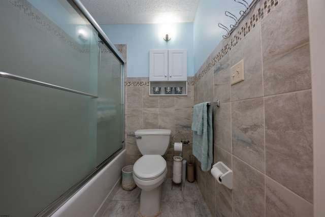 bathroom with tile walls, a textured ceiling, shower / bath combination with glass door, toilet, and tile patterned floors