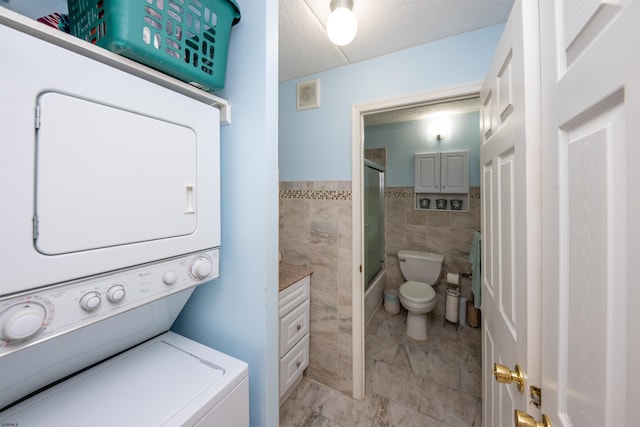 clothes washing area featuring tile walls, stacked washer and dryer, and a textured ceiling