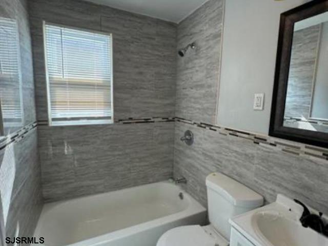 full bathroom featuring tile walls, tiled shower / bath, toilet, and vanity