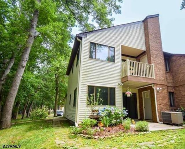 rear view of house with a balcony, central AC unit, a chimney, and a yard