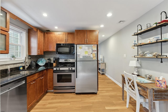 kitchen with light wood-type flooring, dark stone countertops, tasteful backsplash, stainless steel appliances, and sink