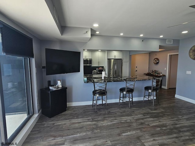 kitchen featuring dark hardwood / wood-style floors, a kitchen breakfast bar, stainless steel appliances, white cabinetry, and dark stone counters