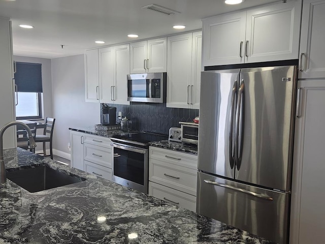 kitchen featuring white cabinets, stainless steel appliances, sink, dark stone counters, and tasteful backsplash