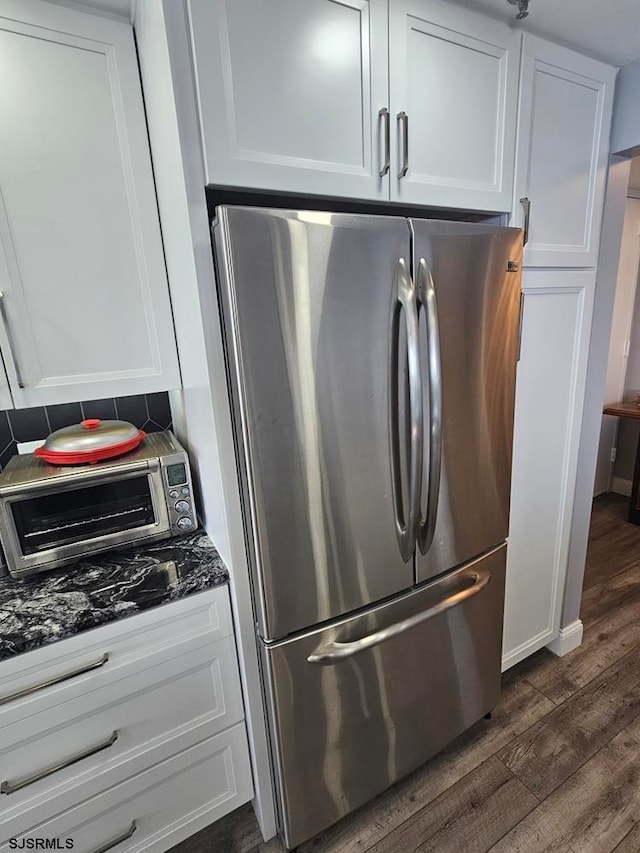 kitchen with dark wood-type flooring, dark stone countertops, stainless steel fridge, and white cabinetry