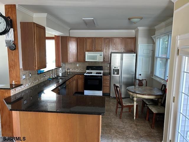 kitchen featuring kitchen peninsula, sink, ornamental molding, backsplash, and white appliances