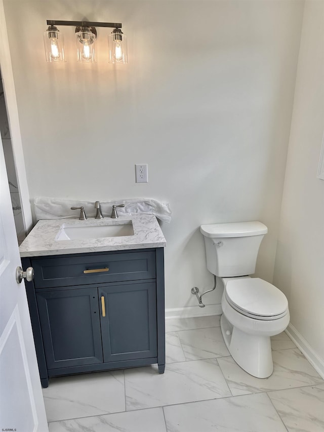 half bathroom with baseboards, marble finish floor, vanity, and toilet