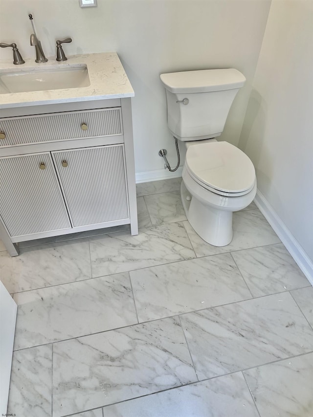 half bath featuring marble finish floor, toilet, vanity, and baseboards