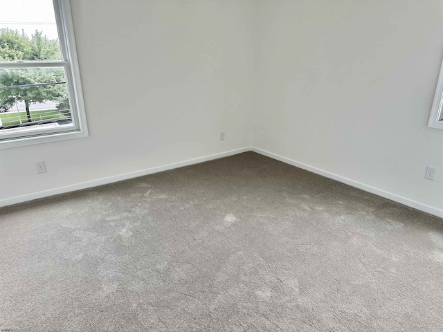 unfurnished room with baseboards and dark colored carpet