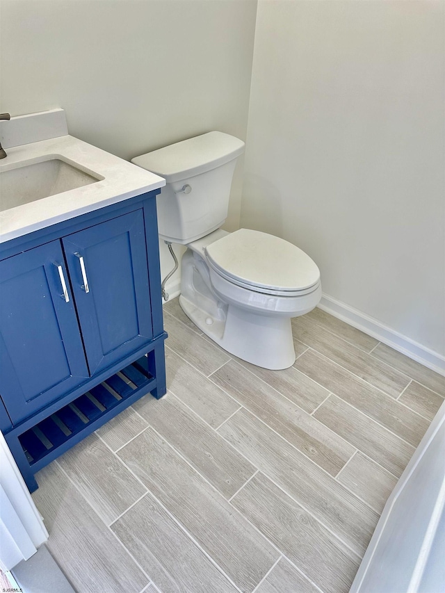 bathroom with vanity, toilet, baseboards, and wood finish floors