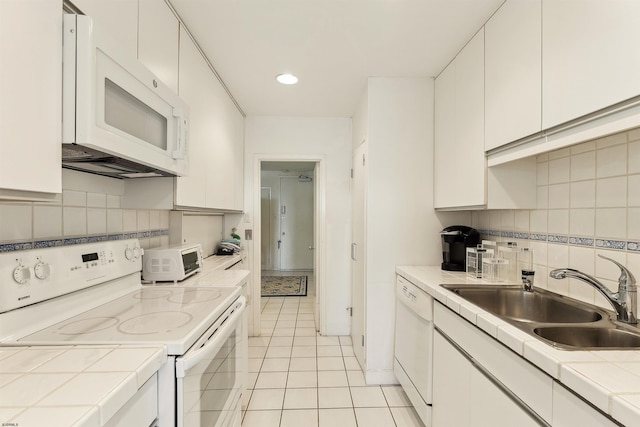 kitchen with white appliances, light tile patterned floors, tile counters, sink, and white cabinets