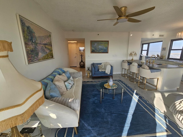 living room with concrete flooring, ceiling fan, sink, and a textured ceiling