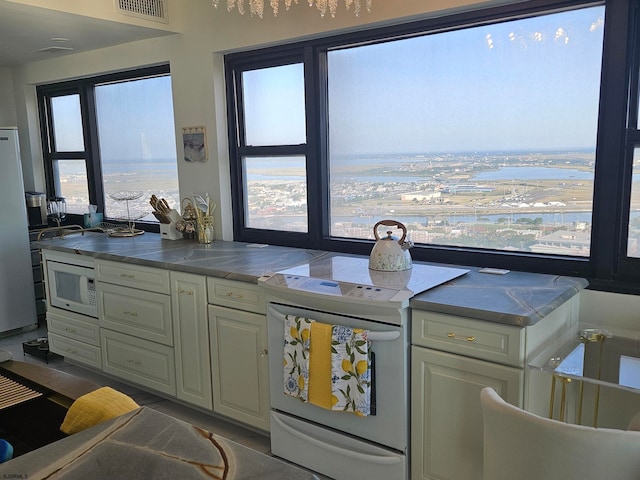 kitchen featuring a water view, white appliances, tile counters, and cream cabinetry