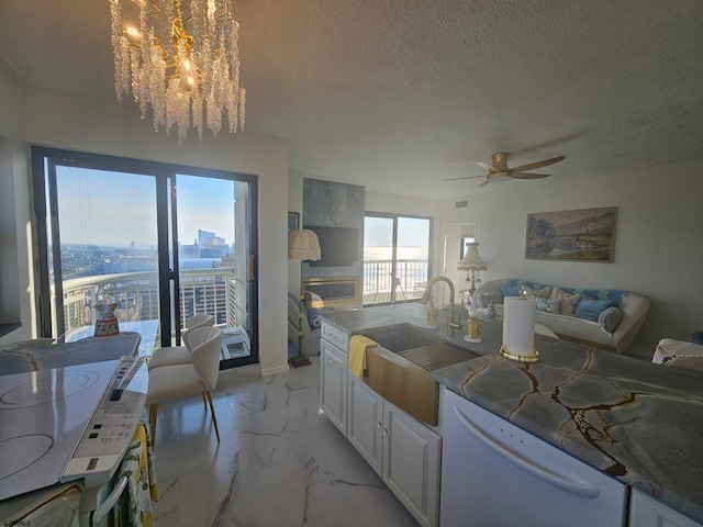 kitchen with white dishwasher, ceiling fan with notable chandelier, white cabinetry, sink, and a textured ceiling