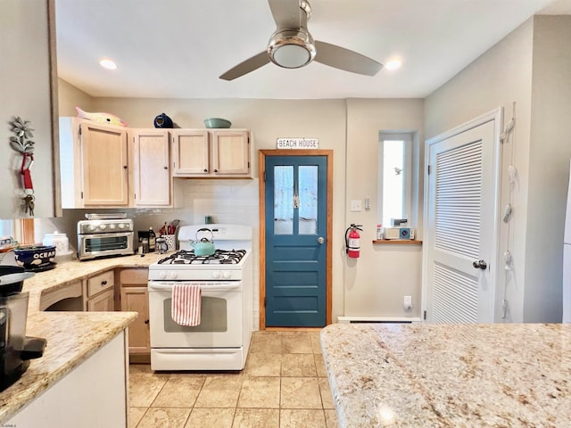 kitchen featuring white range with gas stovetop, light brown cabinetry, light stone countertops, light tile patterned flooring, and ceiling fan