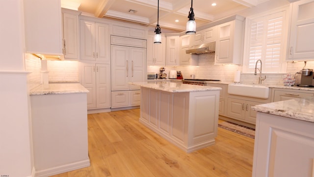 kitchen featuring range hood, decorative light fixtures, light stone counters, sink, and a kitchen island