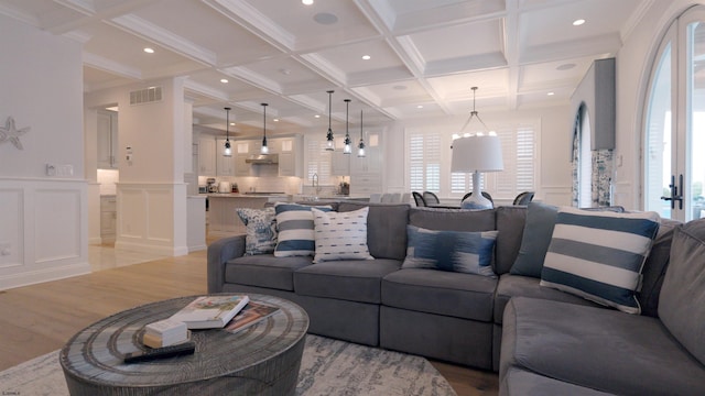 living room with light hardwood / wood-style flooring, coffered ceiling, ornamental molding, and beamed ceiling