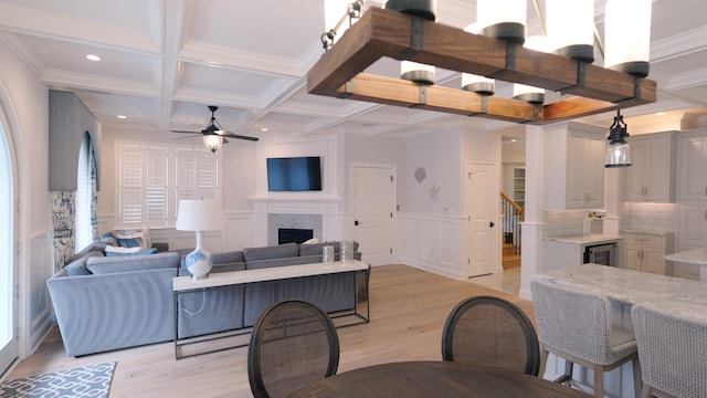 living room featuring light hardwood / wood-style floors, coffered ceiling, a premium fireplace, ceiling fan, and ornamental molding