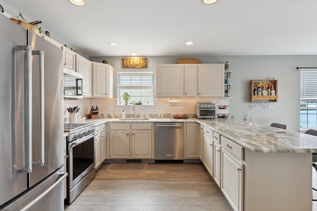 kitchen with light stone counters, light hardwood / wood-style floors, high end appliances, kitchen peninsula, and decorative backsplash