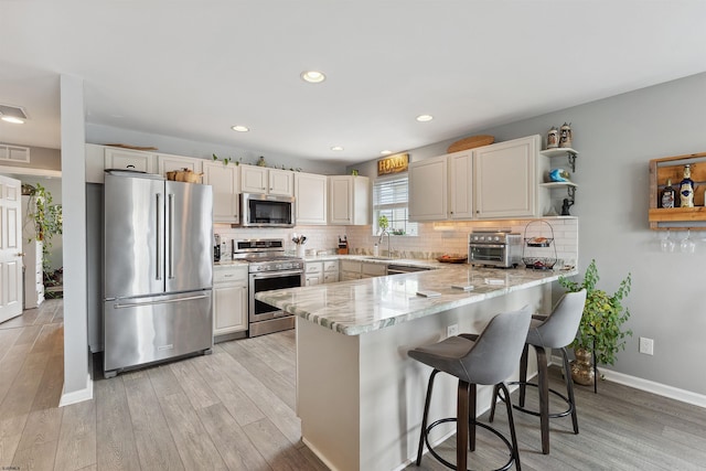 kitchen featuring sink, kitchen peninsula, light hardwood / wood-style flooring, stainless steel appliances, and a kitchen bar