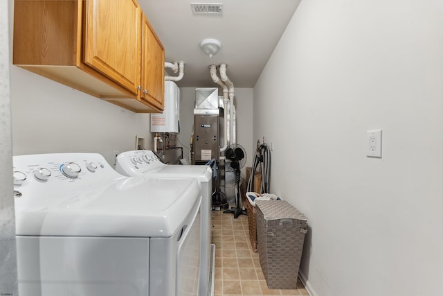 clothes washing area with water heater, washer and dryer, and cabinets