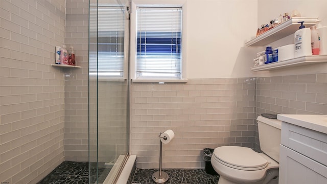 bathroom with tile walls, a shower with shower door, vanity, and toilet