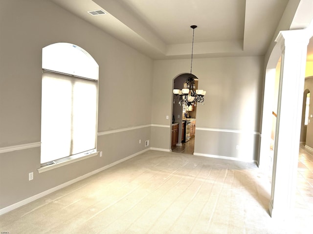 unfurnished dining area featuring light colored carpet, a raised ceiling, an inviting chandelier, and decorative columns