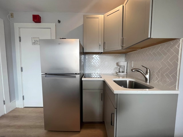 kitchen featuring stainless steel fridge, light hardwood / wood-style floors, gray cabinetry, tasteful backsplash, and sink