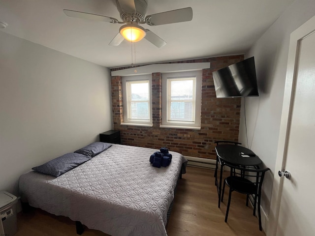 bedroom with baseboard heating, dark hardwood / wood-style flooring, ceiling fan, and brick wall