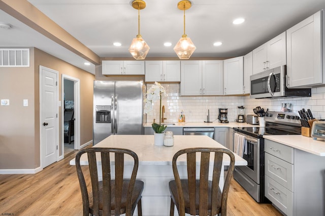 kitchen featuring light hardwood / wood-style flooring, stainless steel appliances, white cabinets, and decorative light fixtures