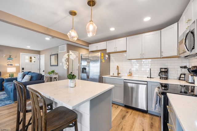 kitchen with sink, light hardwood / wood-style flooring, stainless steel appliances, a kitchen breakfast bar, and decorative light fixtures