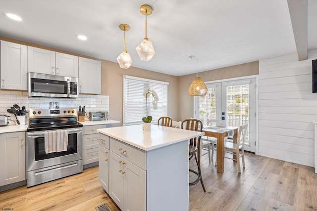 kitchen with light hardwood / wood-style floors, appliances with stainless steel finishes, hanging light fixtures, and a kitchen bar