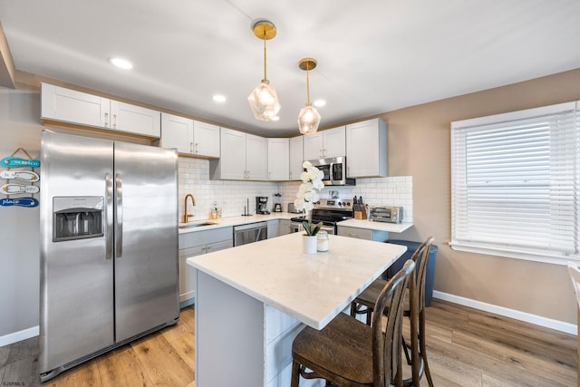 kitchen with stainless steel appliances, a kitchen island, hanging light fixtures, and light wood-type flooring