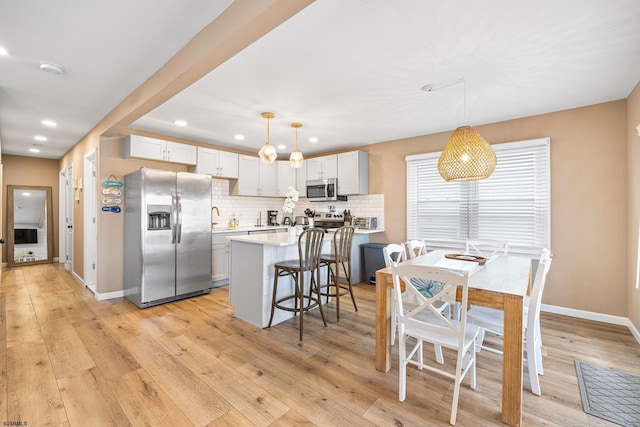 kitchen featuring appliances with stainless steel finishes, hanging light fixtures, light wood-type flooring, and a kitchen island