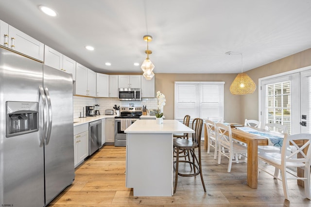 kitchen with pendant lighting, appliances with stainless steel finishes, light wood-type flooring, and white cabinetry