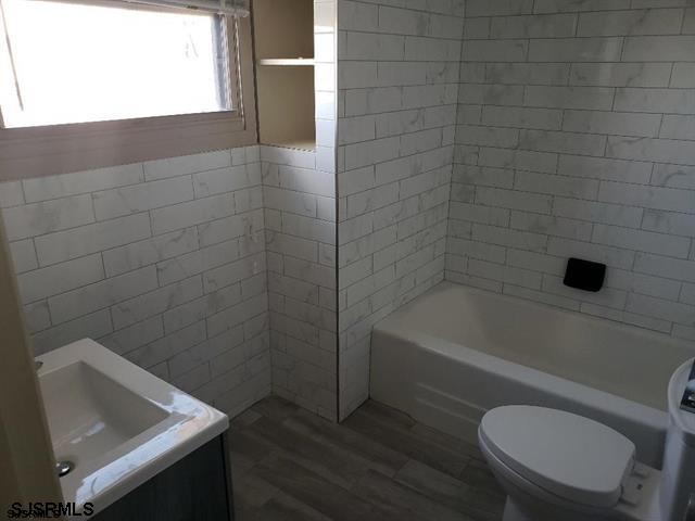 full bathroom with tile walls, vanity, tiled shower / bath combo, hardwood / wood-style flooring, and toilet