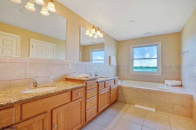 bathroom with an inviting chandelier, tile patterned floors, a relaxing tiled tub, and vanity