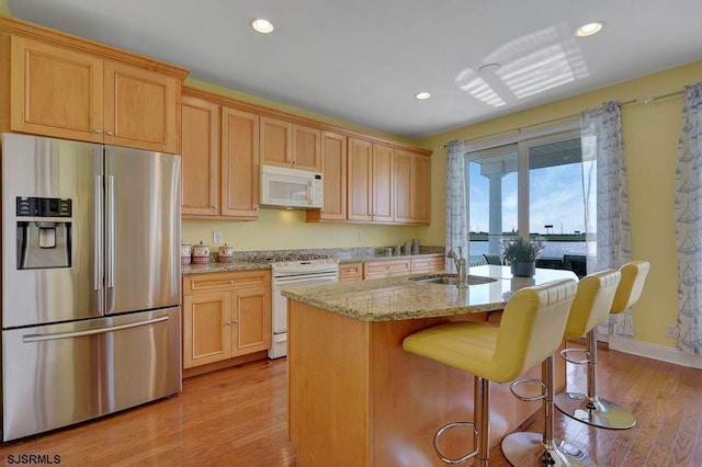 kitchen with sink, light hardwood / wood-style flooring, white appliances, a center island with sink, and light stone countertops