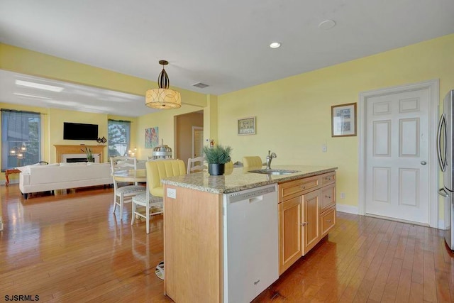 kitchen with light stone counters, a kitchen island with sink, sink, decorative light fixtures, and white dishwasher