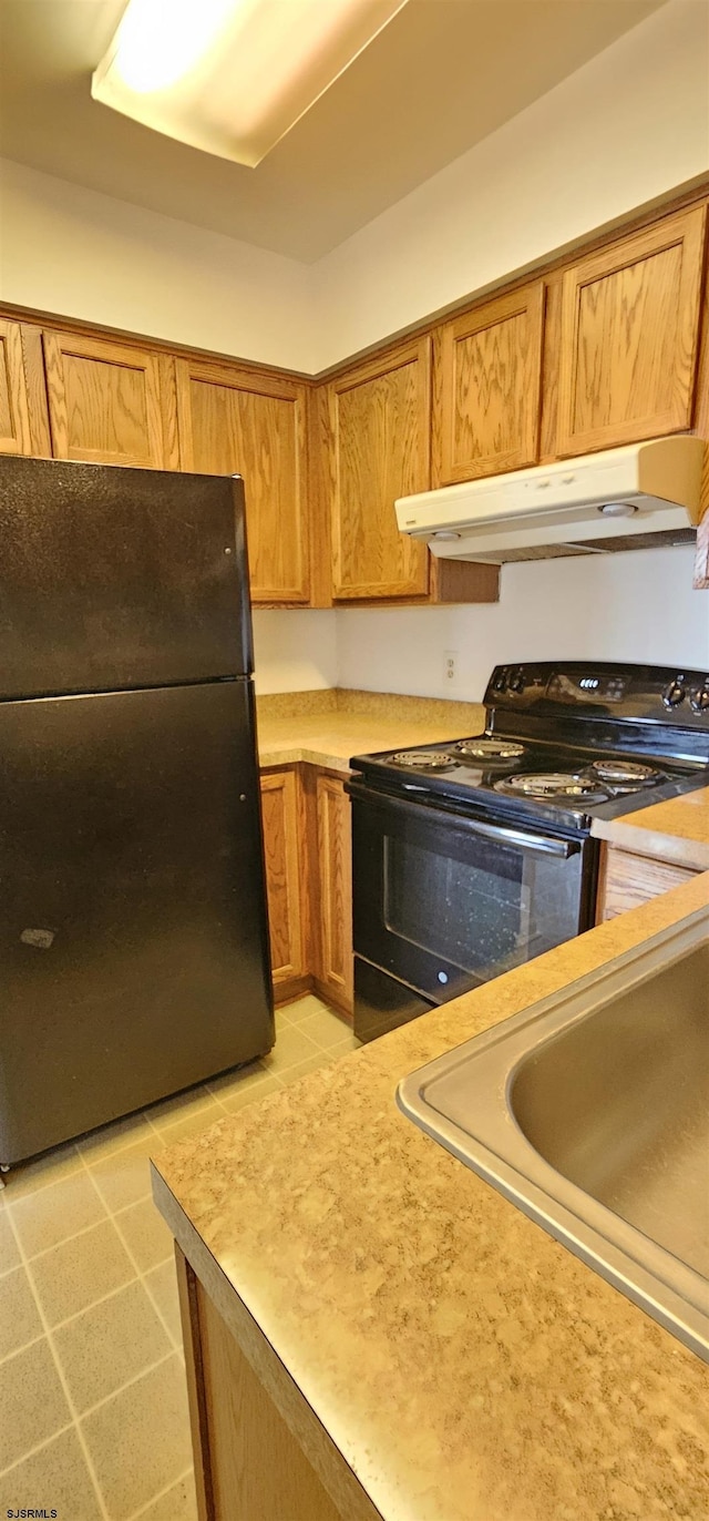 kitchen with under cabinet range hood, brown cabinetry, a sink, and black appliances