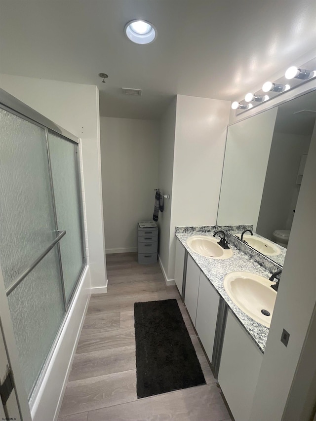 full bathroom featuring vanity, hardwood / wood-style floors, enclosed tub / shower combo, and toilet